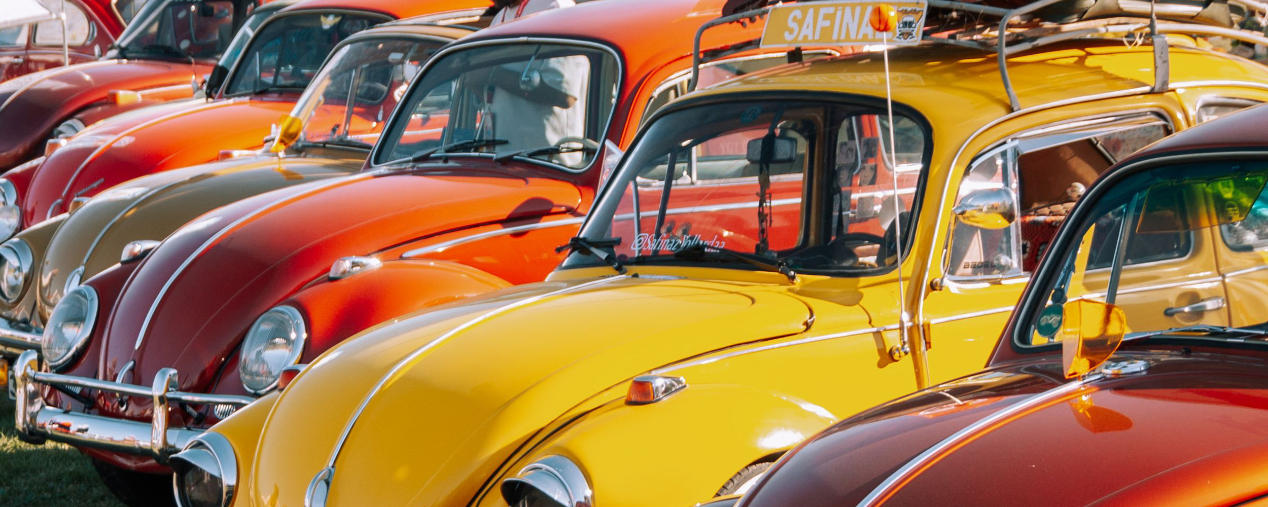 Lineup of colorful vintage Beetles parked on cobblestone beside a yellow wall